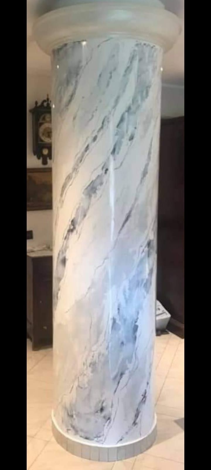 Colonna in marmo bianco con venature grigie. All'interno, sullo sfondo di una stanza arredata.