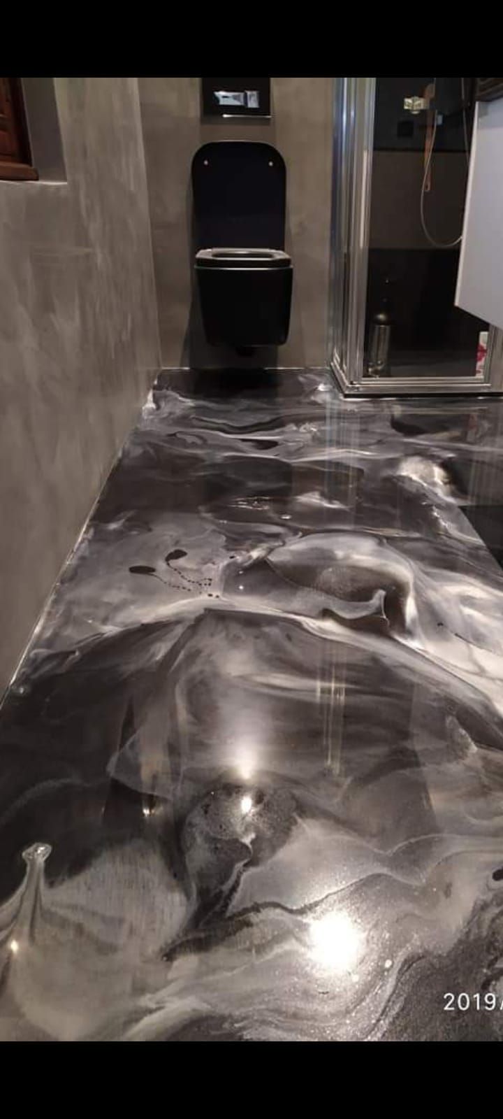 Bagno con pavimento in resina epossidica nera e argento, WC nero ed elettrodomestico color argento metallizzato.