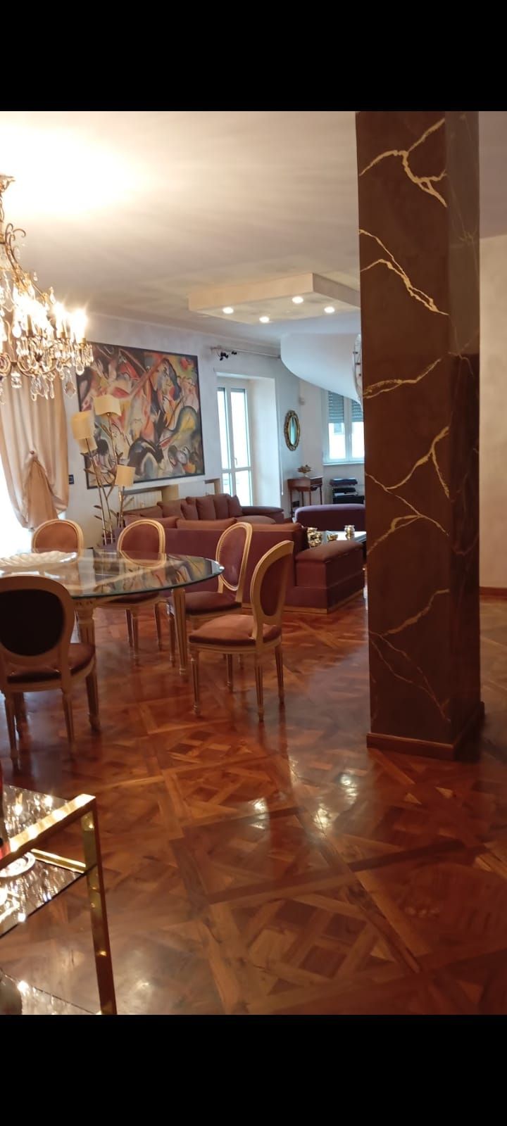 Interni lussuosi con pavimento in legno lucido, dettagli dorati e un grande lampadario. La zona pranzo e il soggiorno sono visibili.