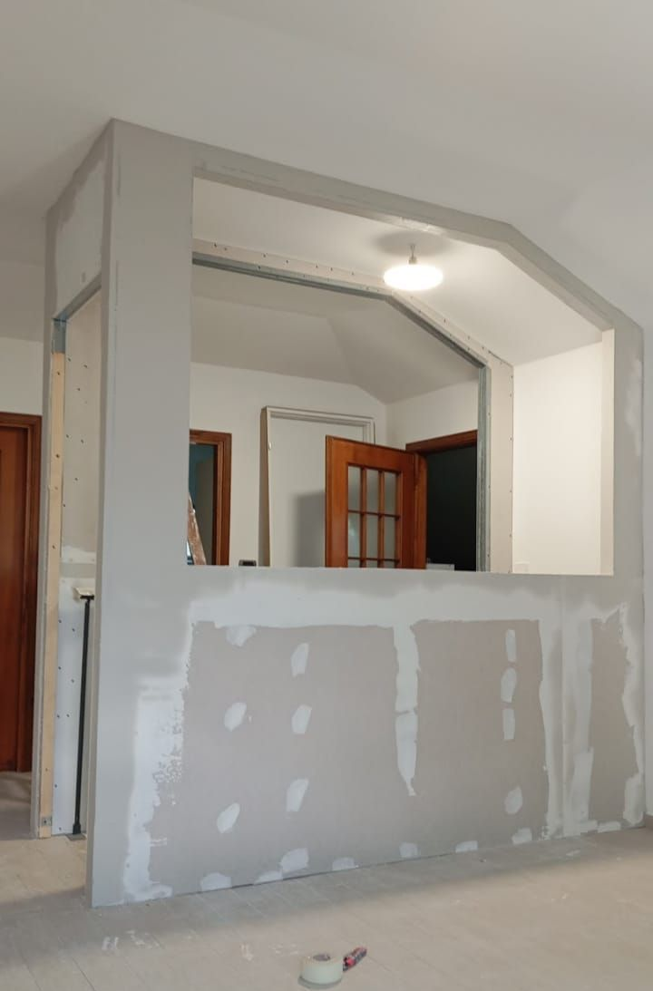 Il cartongesso ricopre parzialmente una parete con un'apertura. Ambiente interno con porte e lampada visibili.