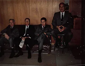 Older photo of Mynatt Funeral Home, Inc. staff members three are sitting on couch and the forth sitting on stool