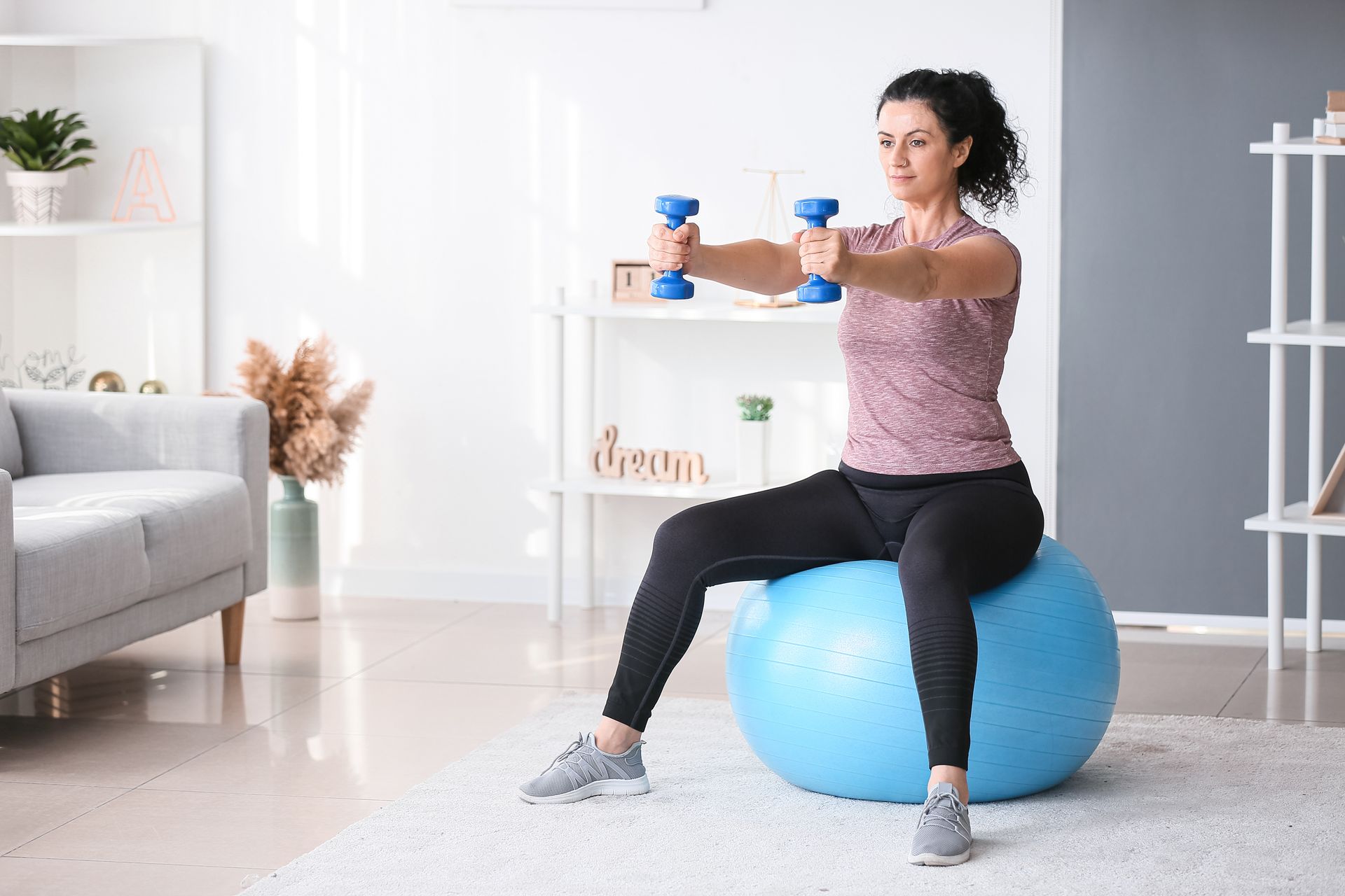 Woman exercising with dumbbells while seated on a blue exercise ball.