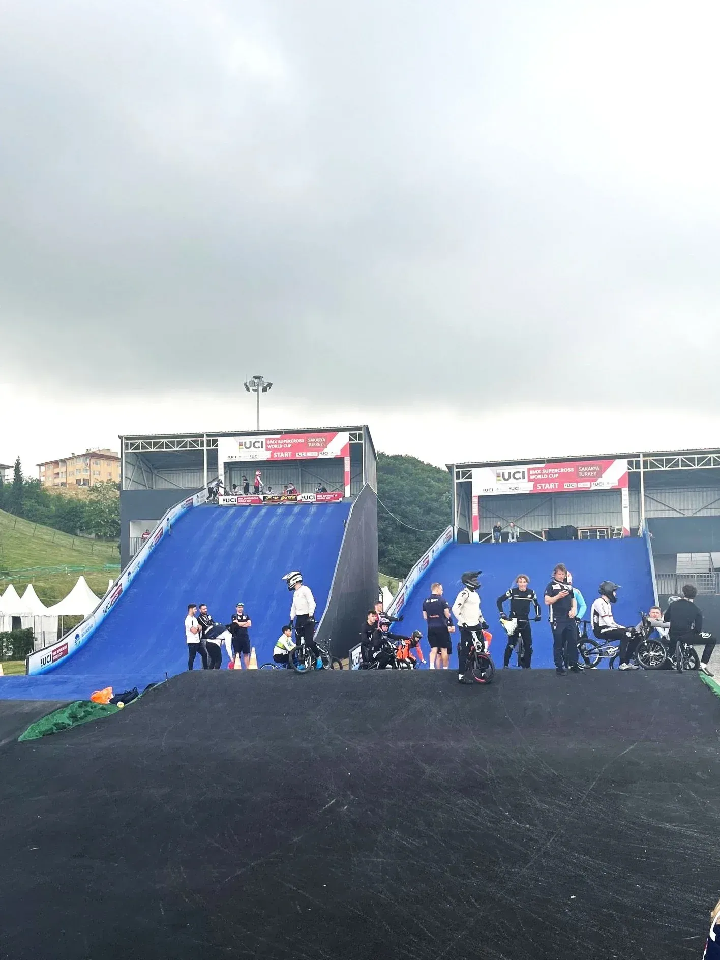 BMX ramp with athletes, some in wheelchairs, at the starting line under a cloudy sky.
