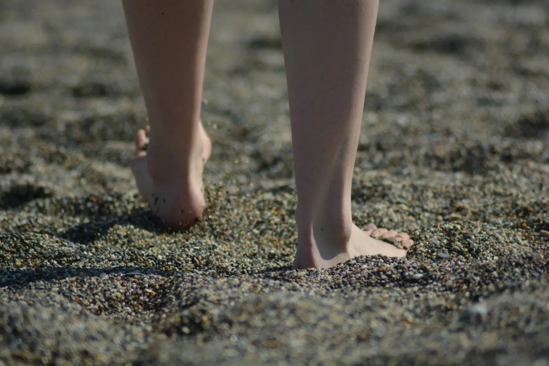 Bare feet walking on a textured, sandy surface.