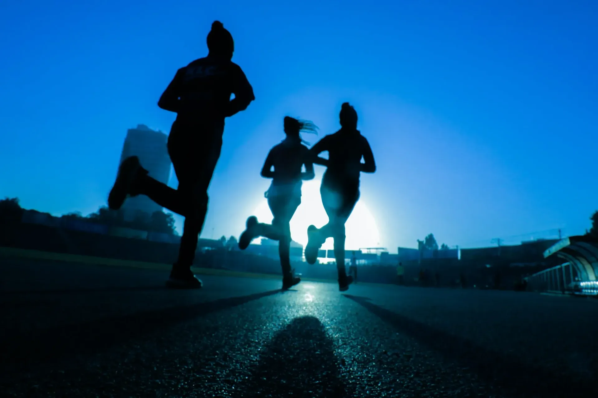 Silhouetted runners on track against a bright blue sky.