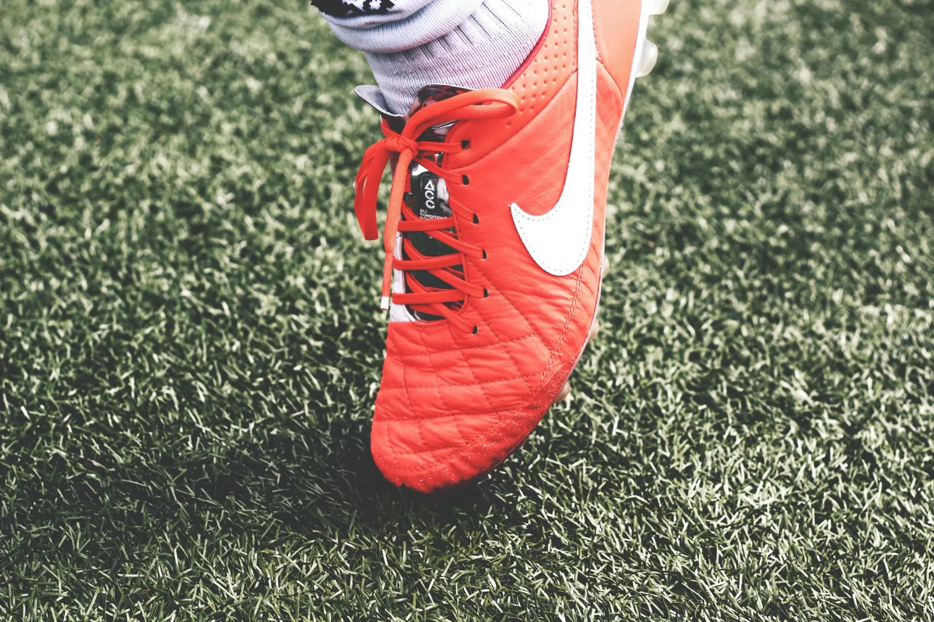 Orange Nike soccer cleat on green artificial turf.