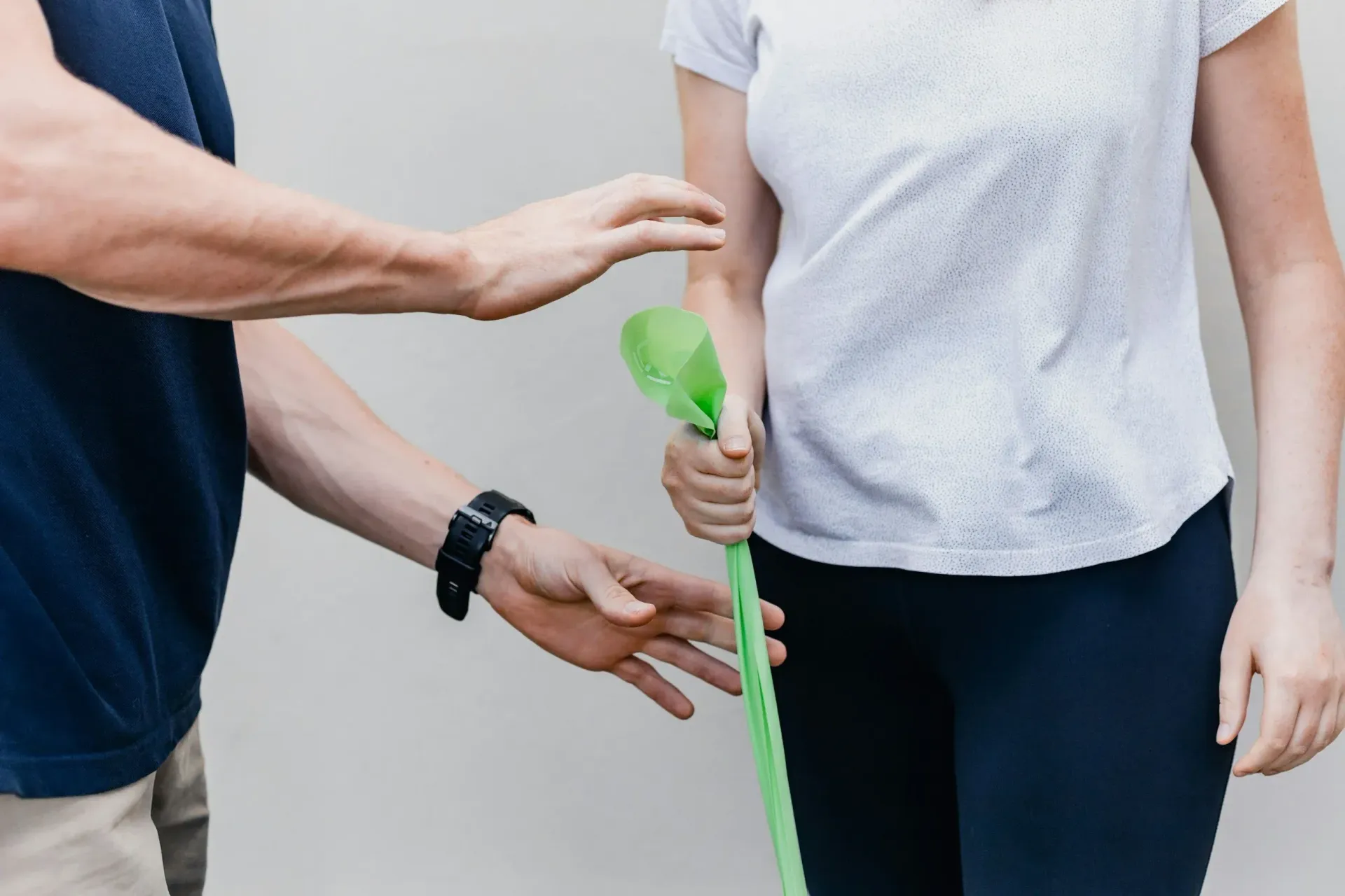 Person guiding another holding a green stick; hands visible, indoors, plain background.
