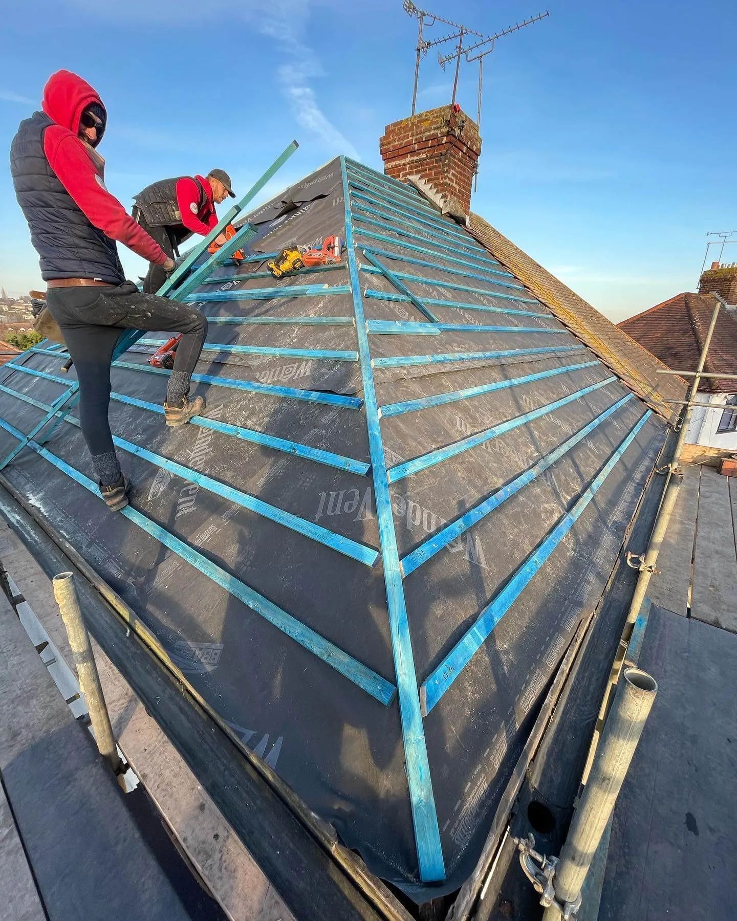 Two roofers installing roofing material on a house roof under a clear blue sky.