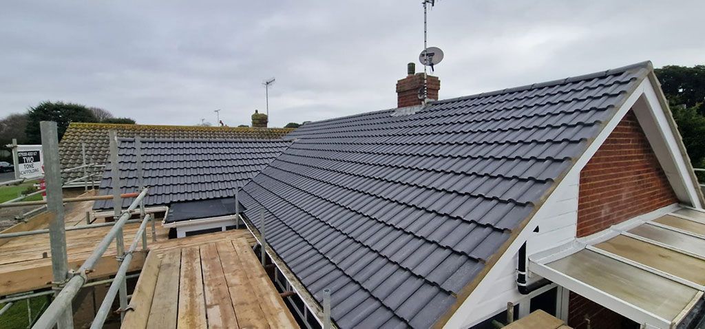 House roof under construction, with gray tiles installed, scaffolding present, overcast sky.