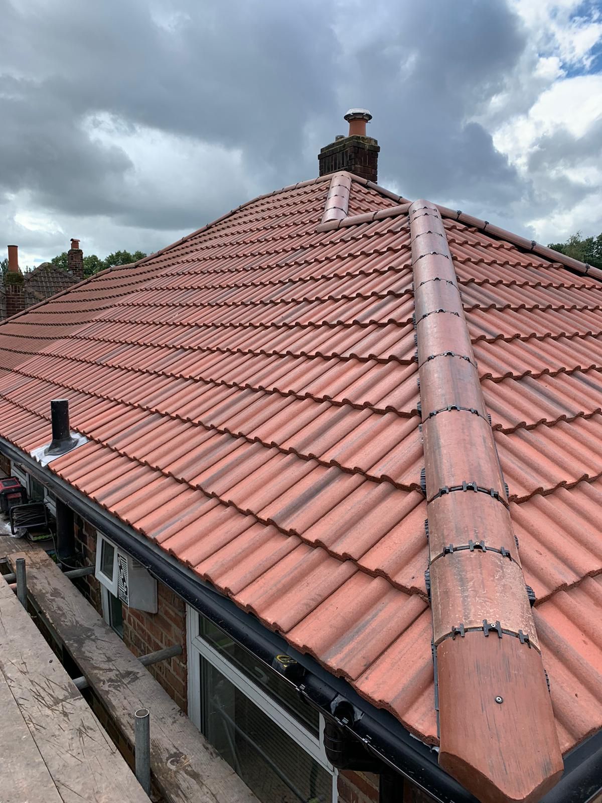 Red tiled roof with copper flashing and black guttering on a brick building, overcast sky.