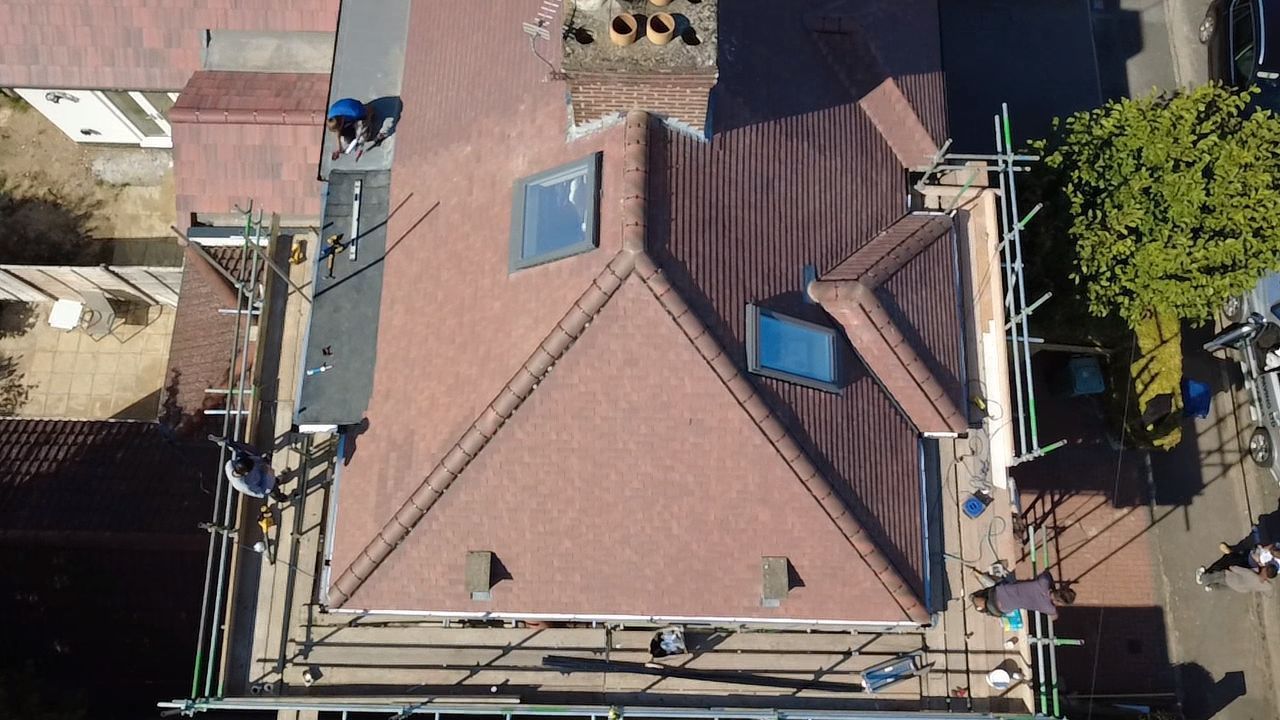 Overhead view of a house roof, scaffolding, and skylights; roofers working in sunlight.