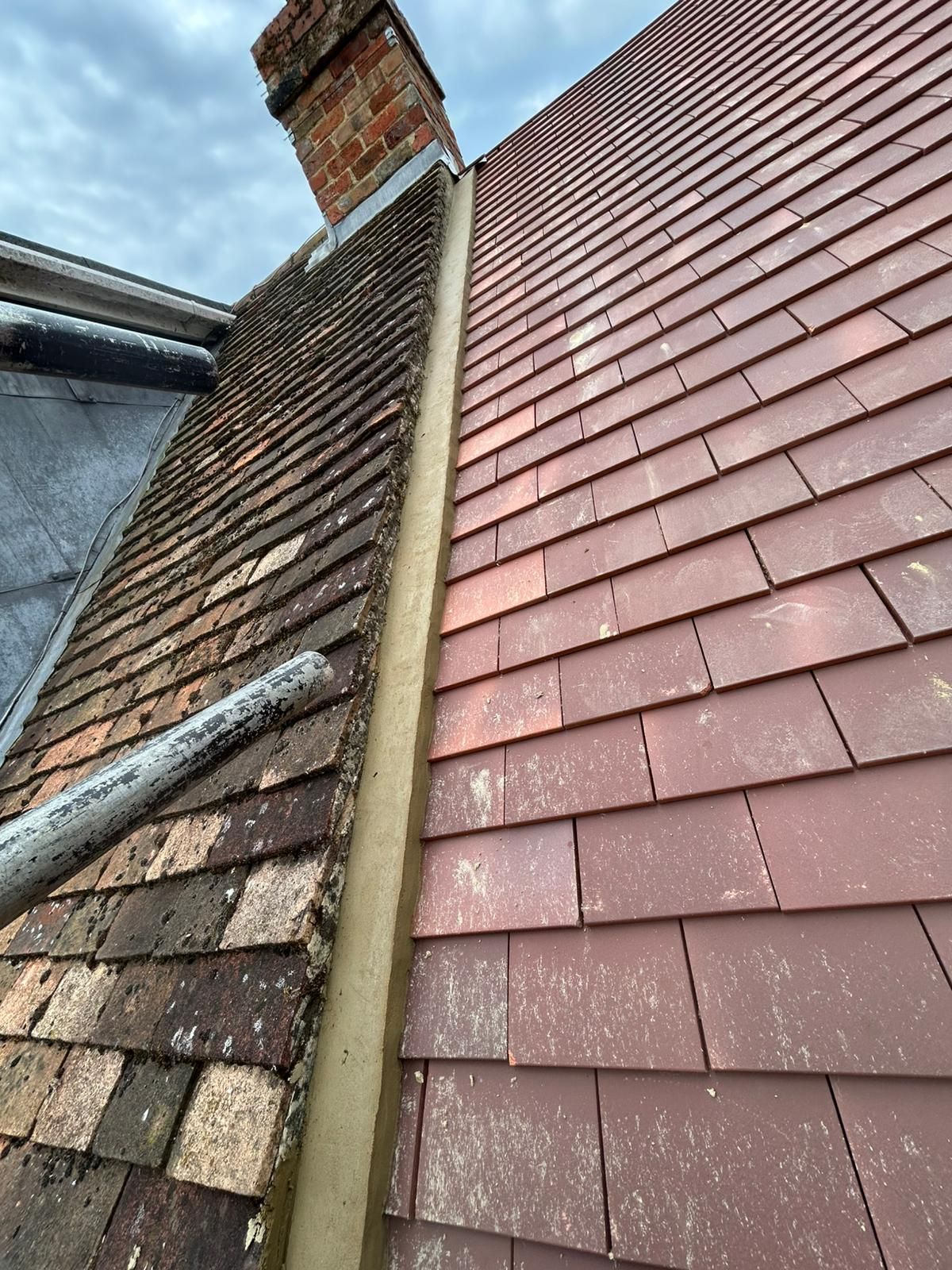 Roofs of a house with different colored tiles, chimney, and gutter. One roof is weathered and the other is newer.