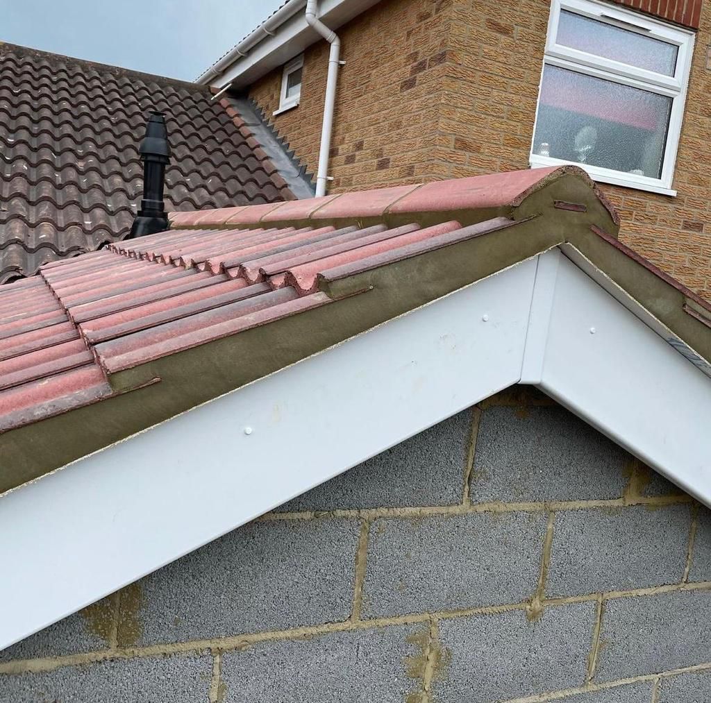 Roof of a house with red tiles, a white trim, and a brick wall.