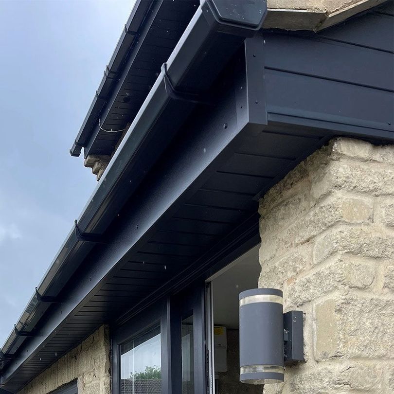 Black gutters and soffits on a stone building, with a window and outdoor light.