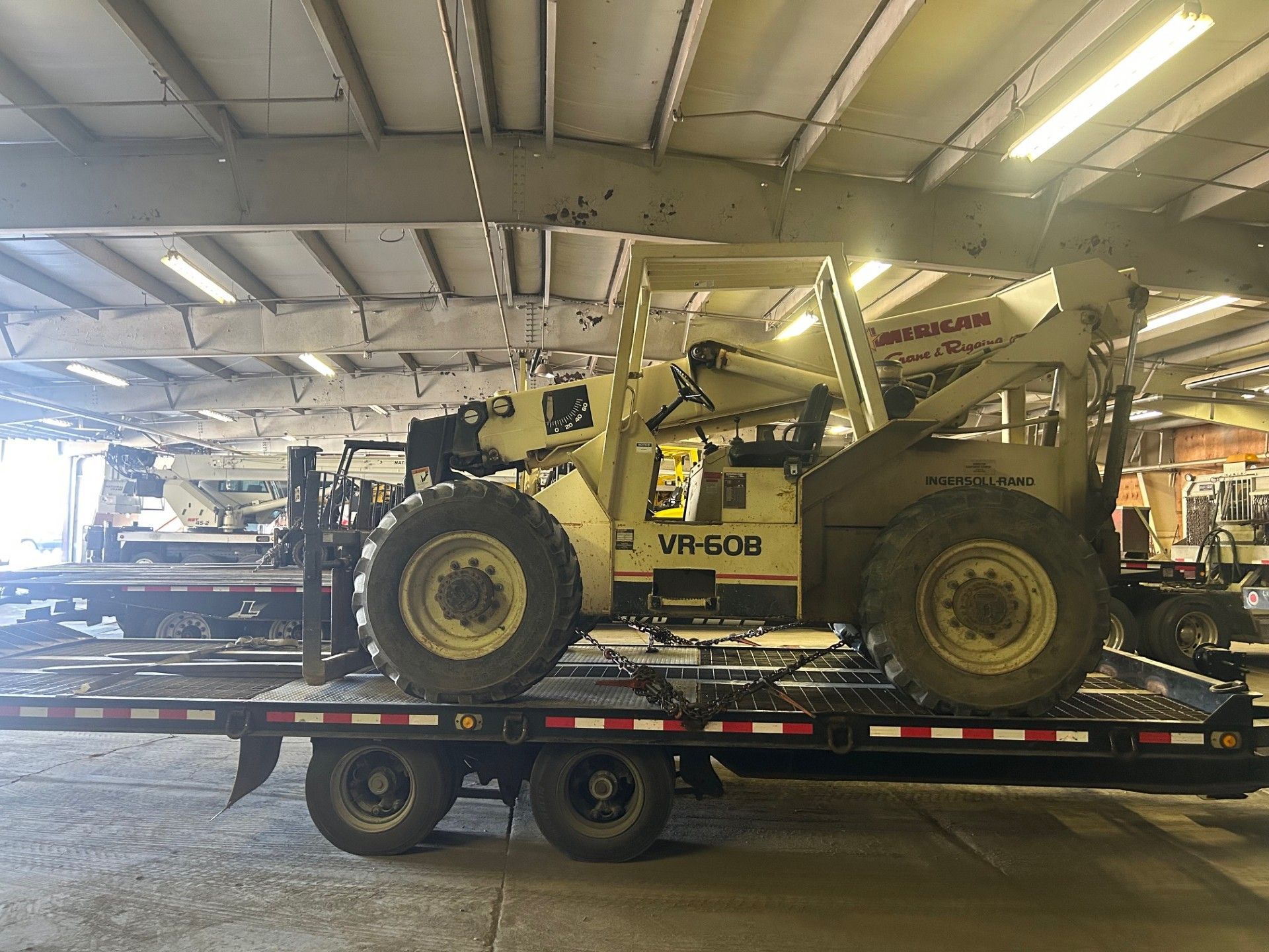 Red telescopic forklift on a construction site, next to yellow and white barriers.