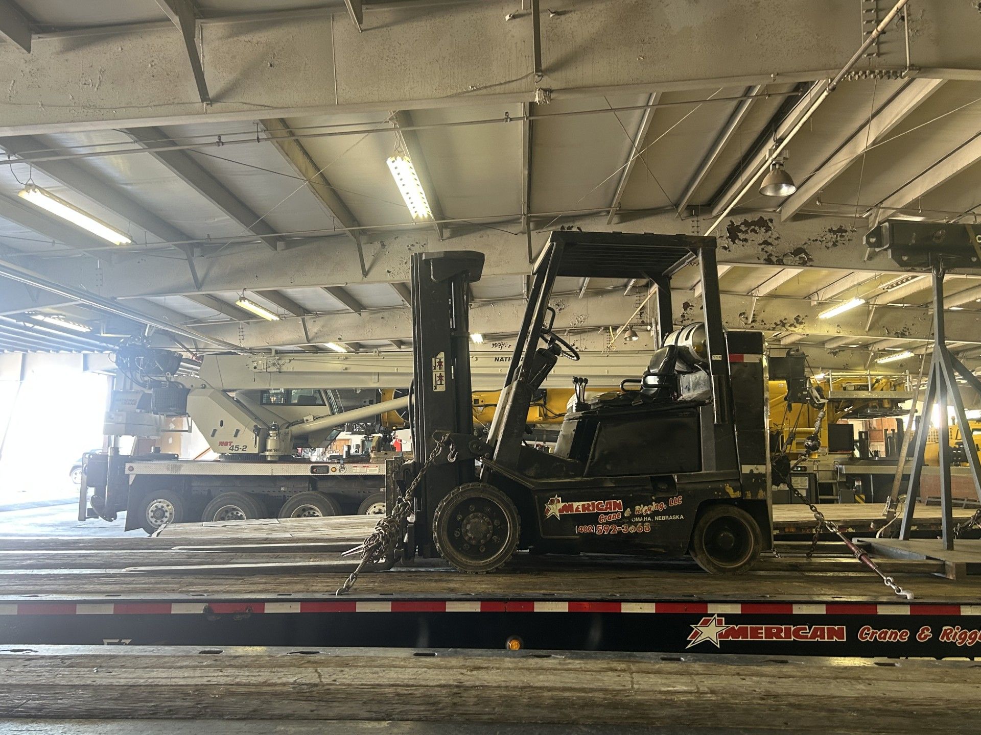 Forklift loading a large, yellow object onto a flatbed trailer. Men nearby, under a blue sky.