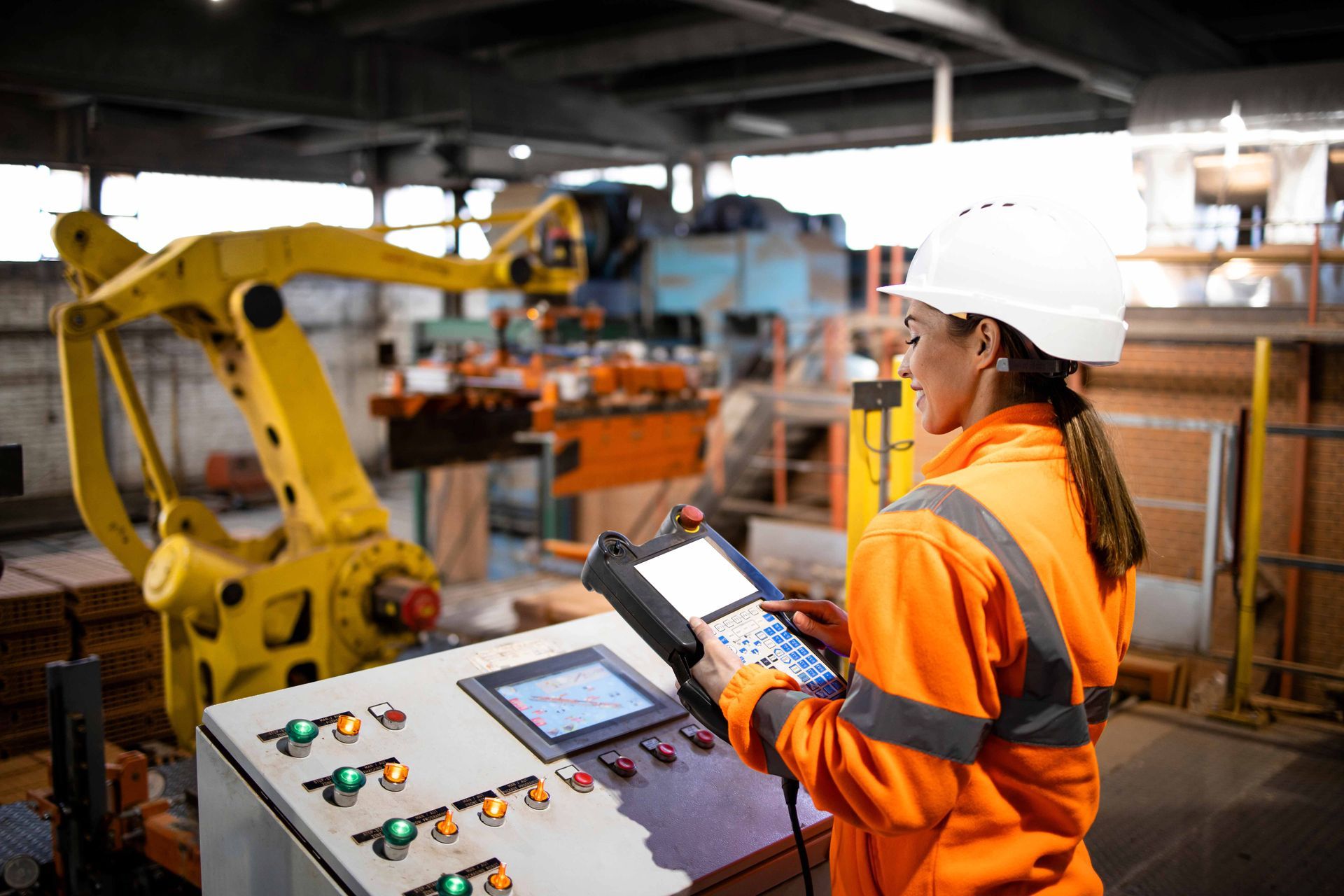 Worker operates a control panel beside a large yellow robotic arm in an industrial facility.