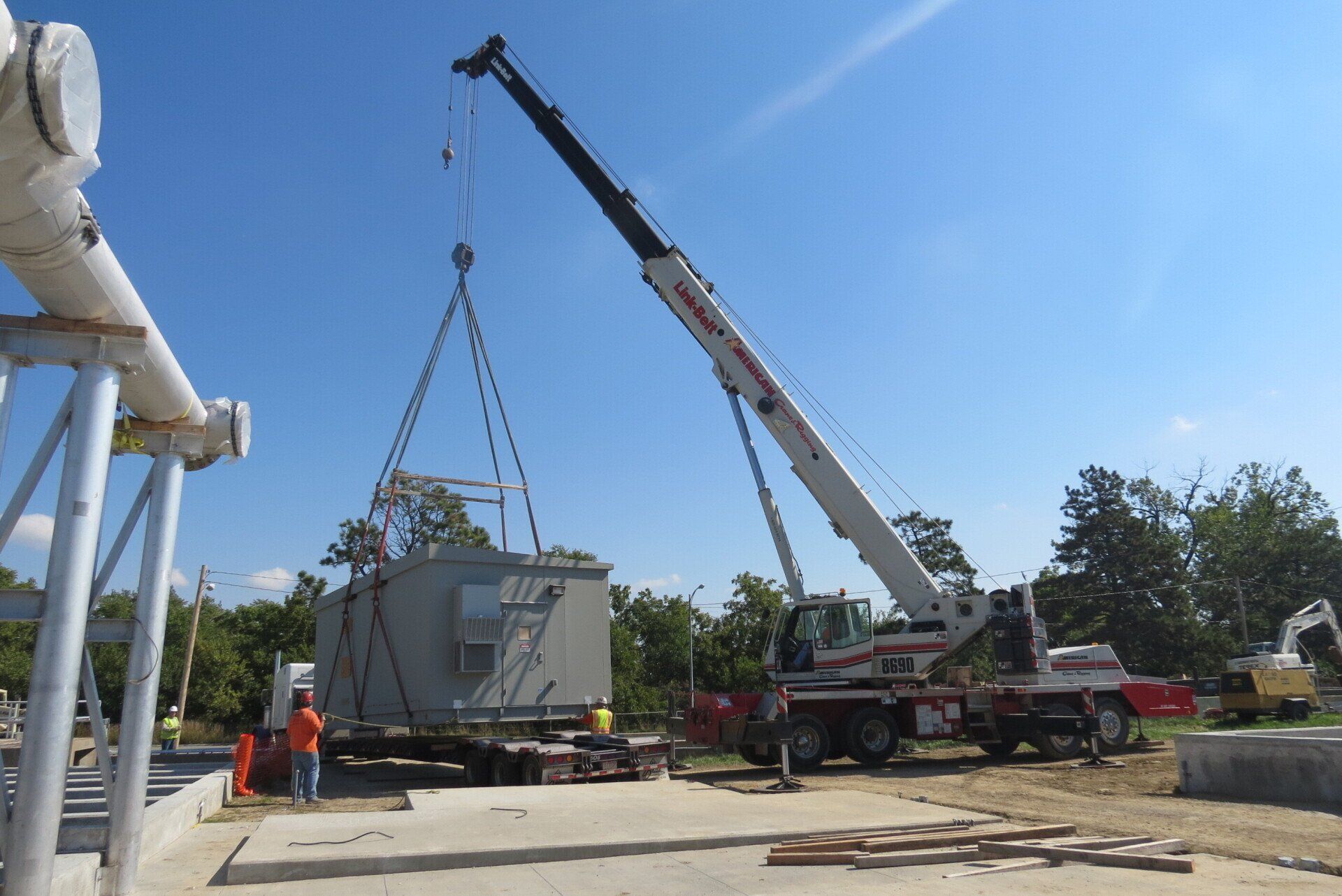 A green crane lifting a red and green train engine against a blue sky.