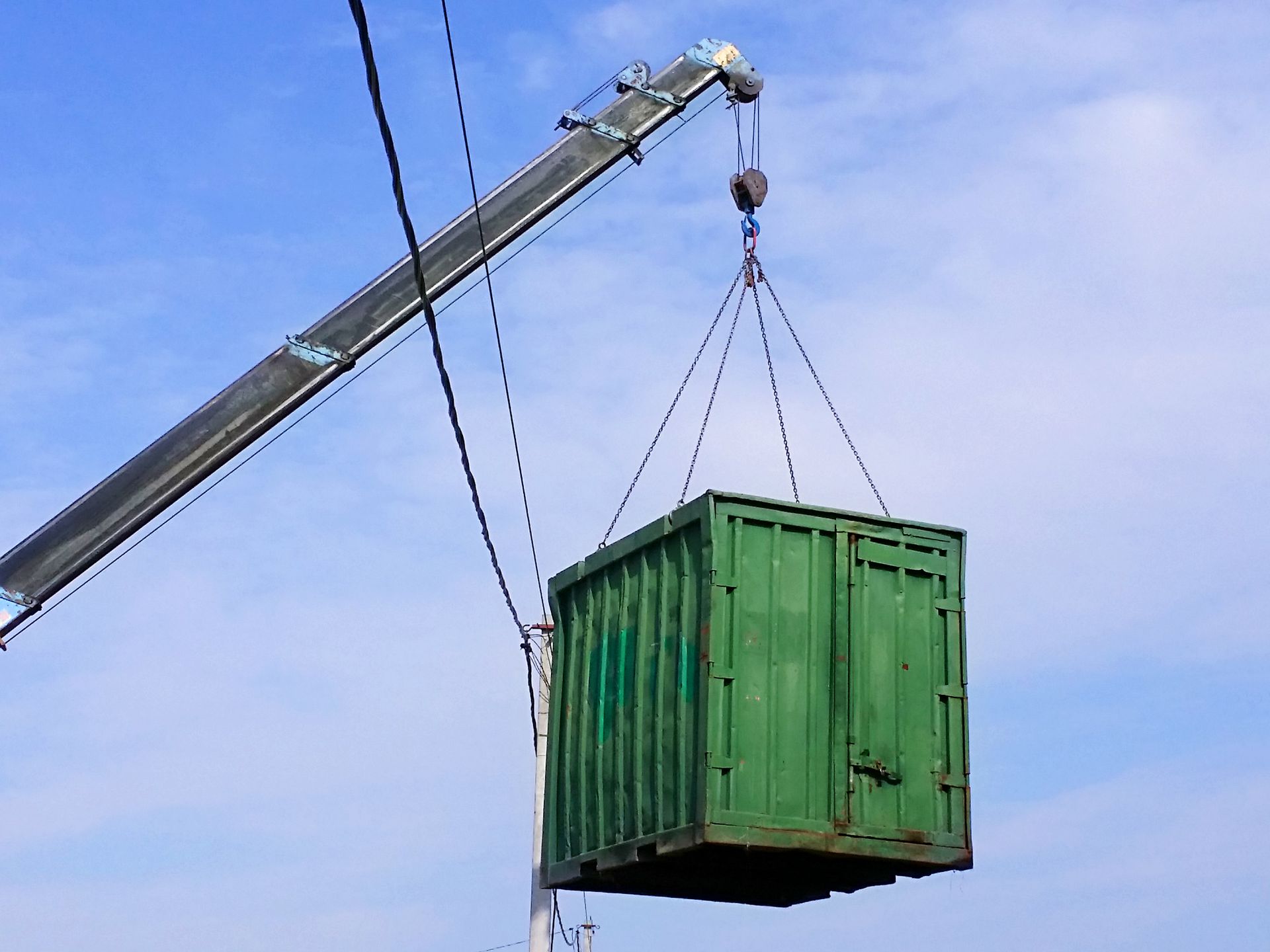 A green shipping container is being lifted by a crane against a blue sky.
