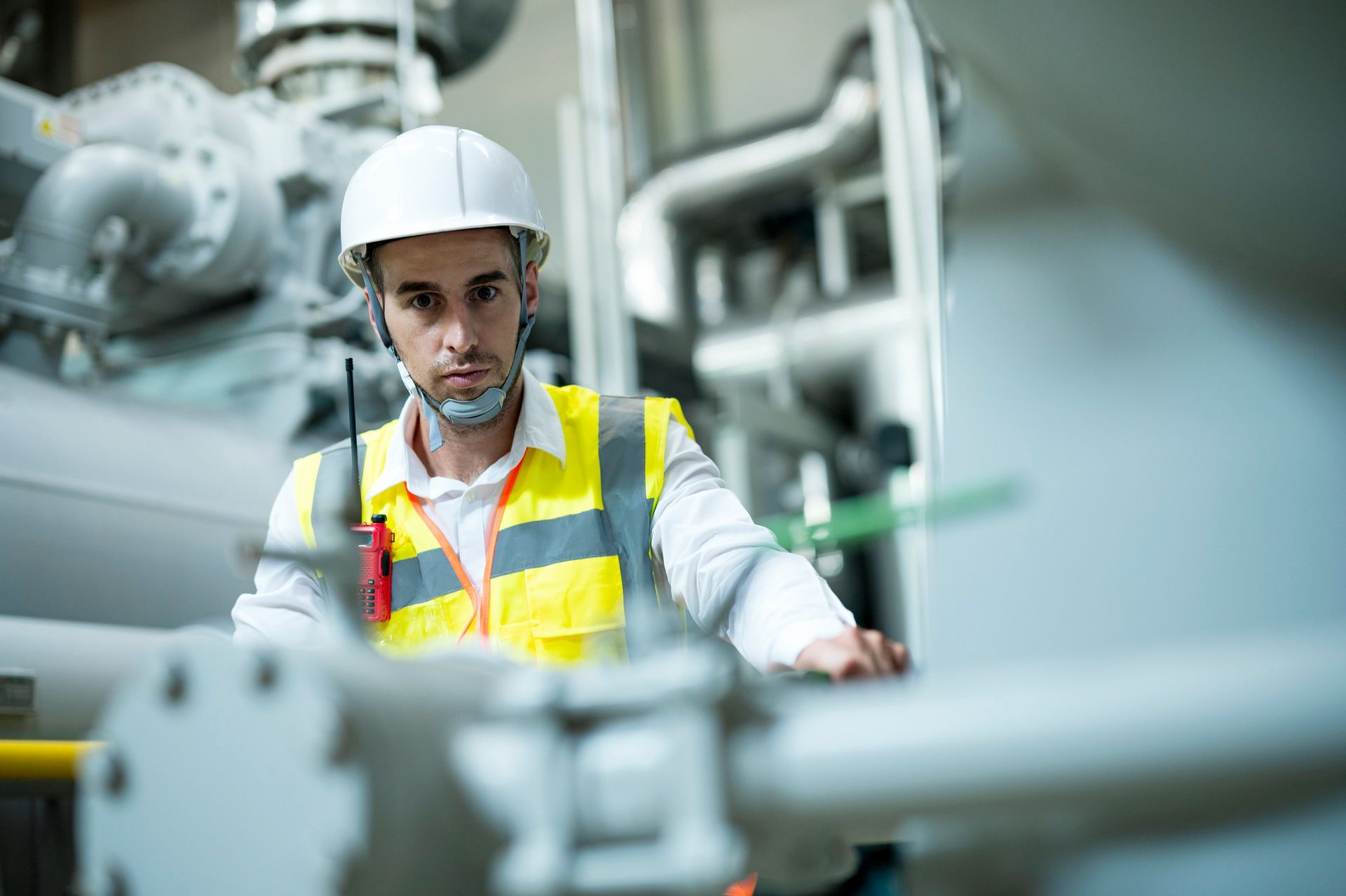 Man in hard hat and safety vest inspecting machinery in an industrial setting.