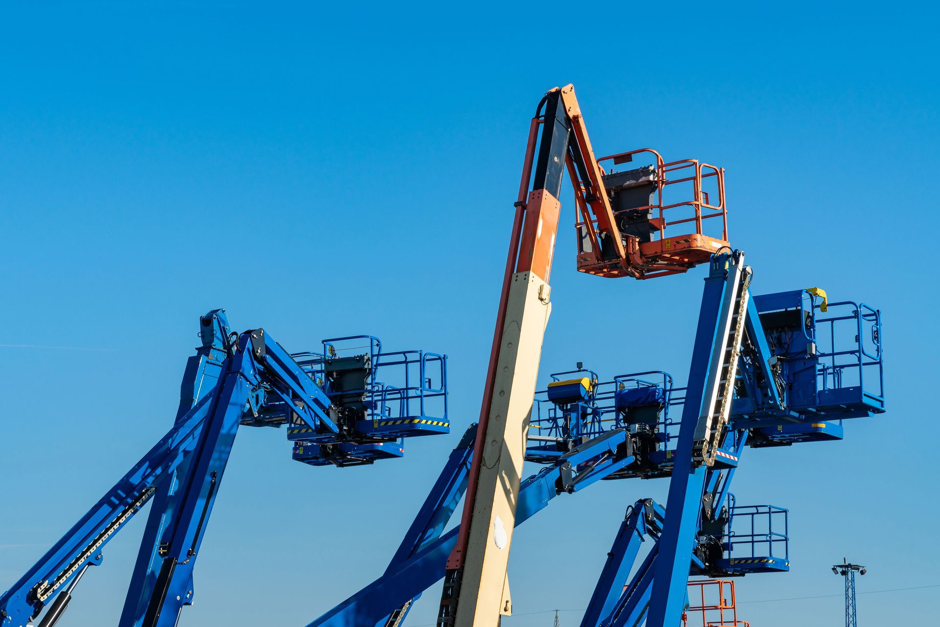 Blue and orange aerial lifts against a clear, blue sky.