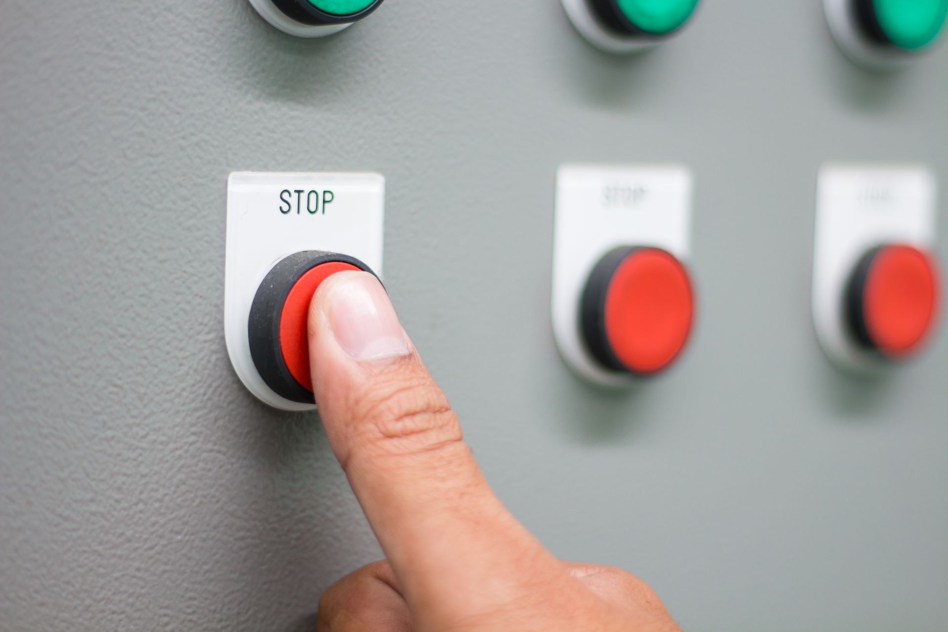 Person's finger pressing a red stop button on a gray control panel.