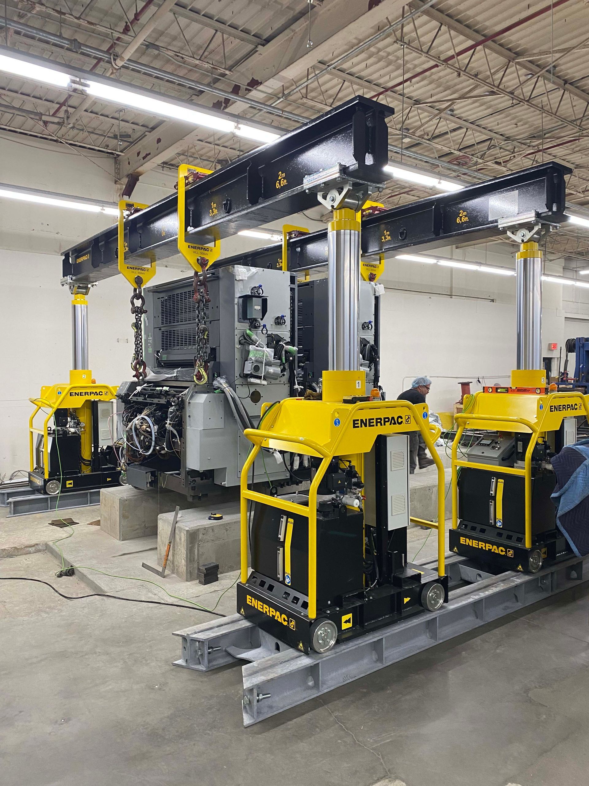 A lifting gantry system hoisting a large industrial machine using yellow Enerpac units