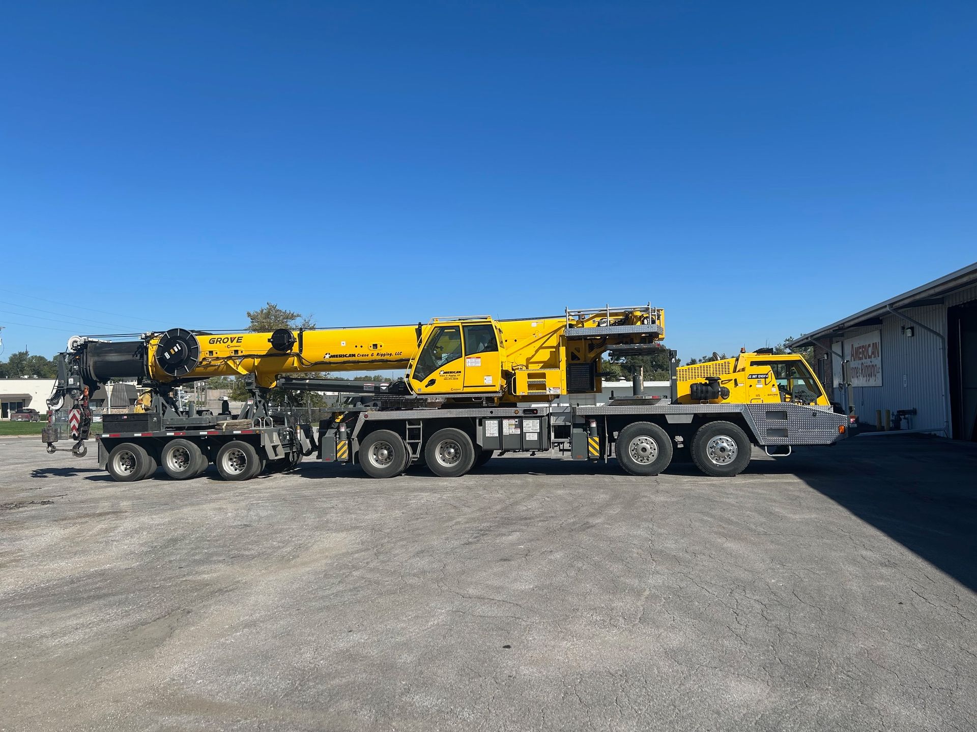 A crane lifting a large, silver MRI machine towards a modern building with a dark facade.