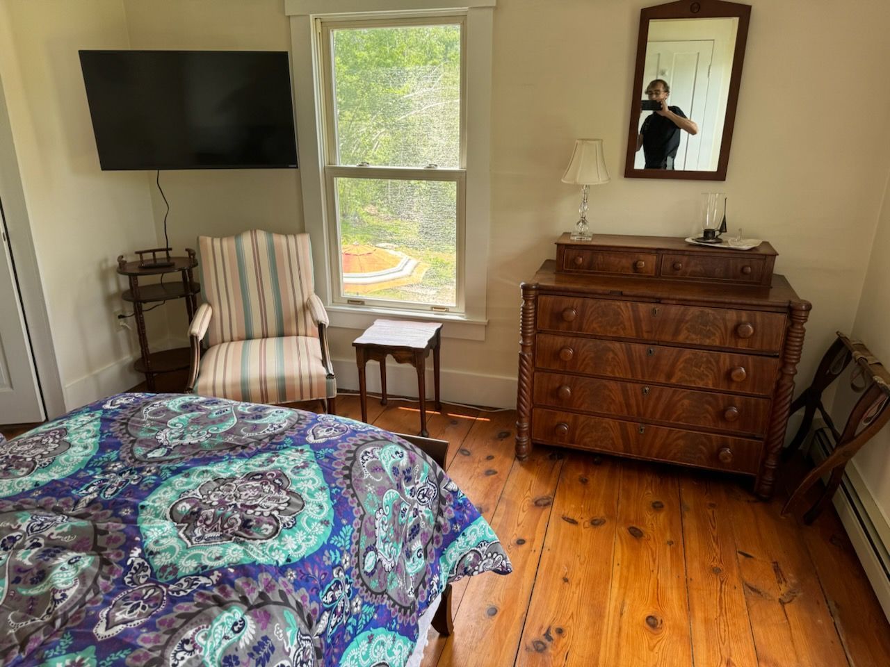 Bedroom with bed, dresser, chair, window, and TV. A person is reflected in a mirror.