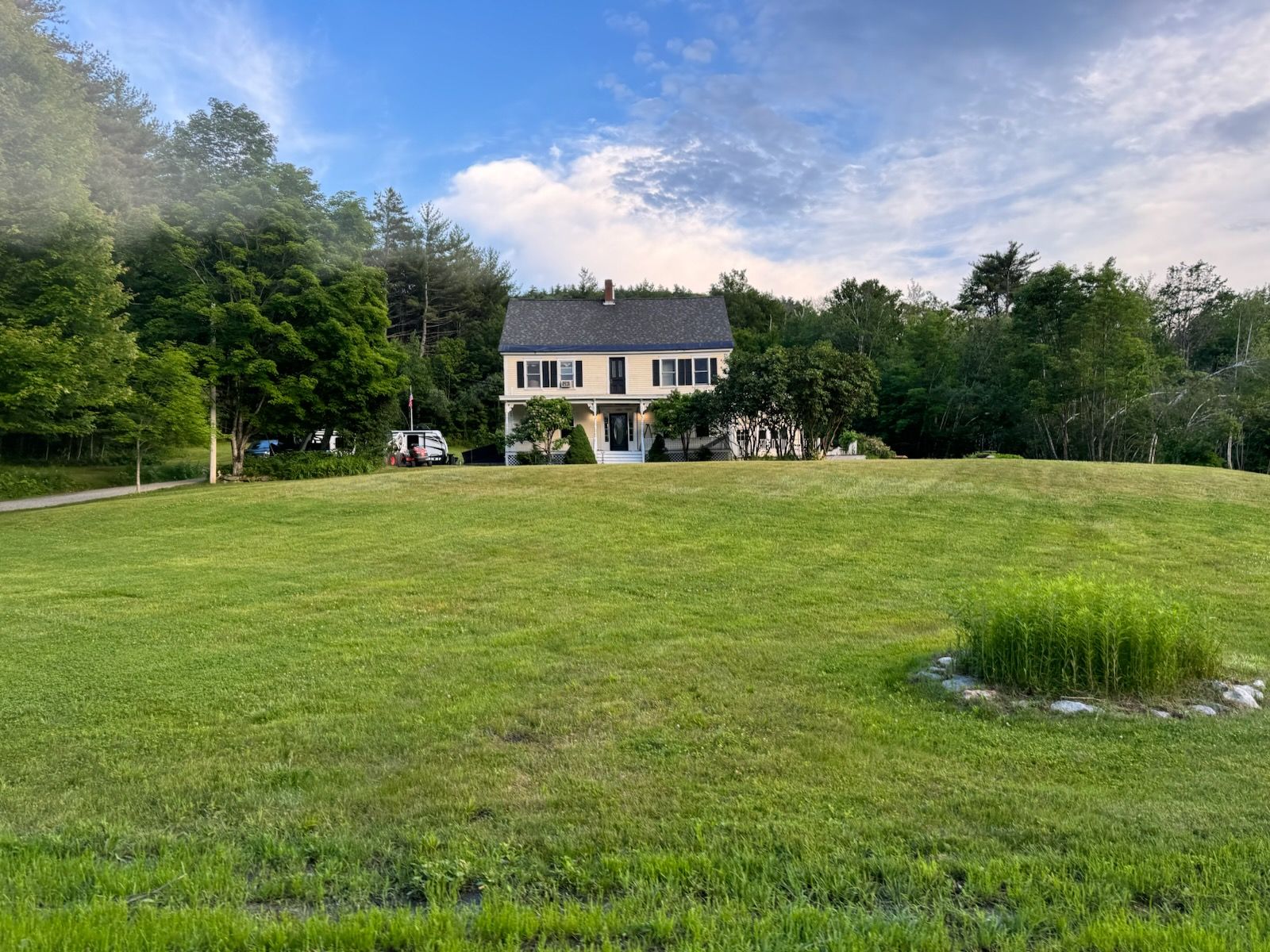 Yellow house with black roof, in a clearing of grass, surrounded by trees.