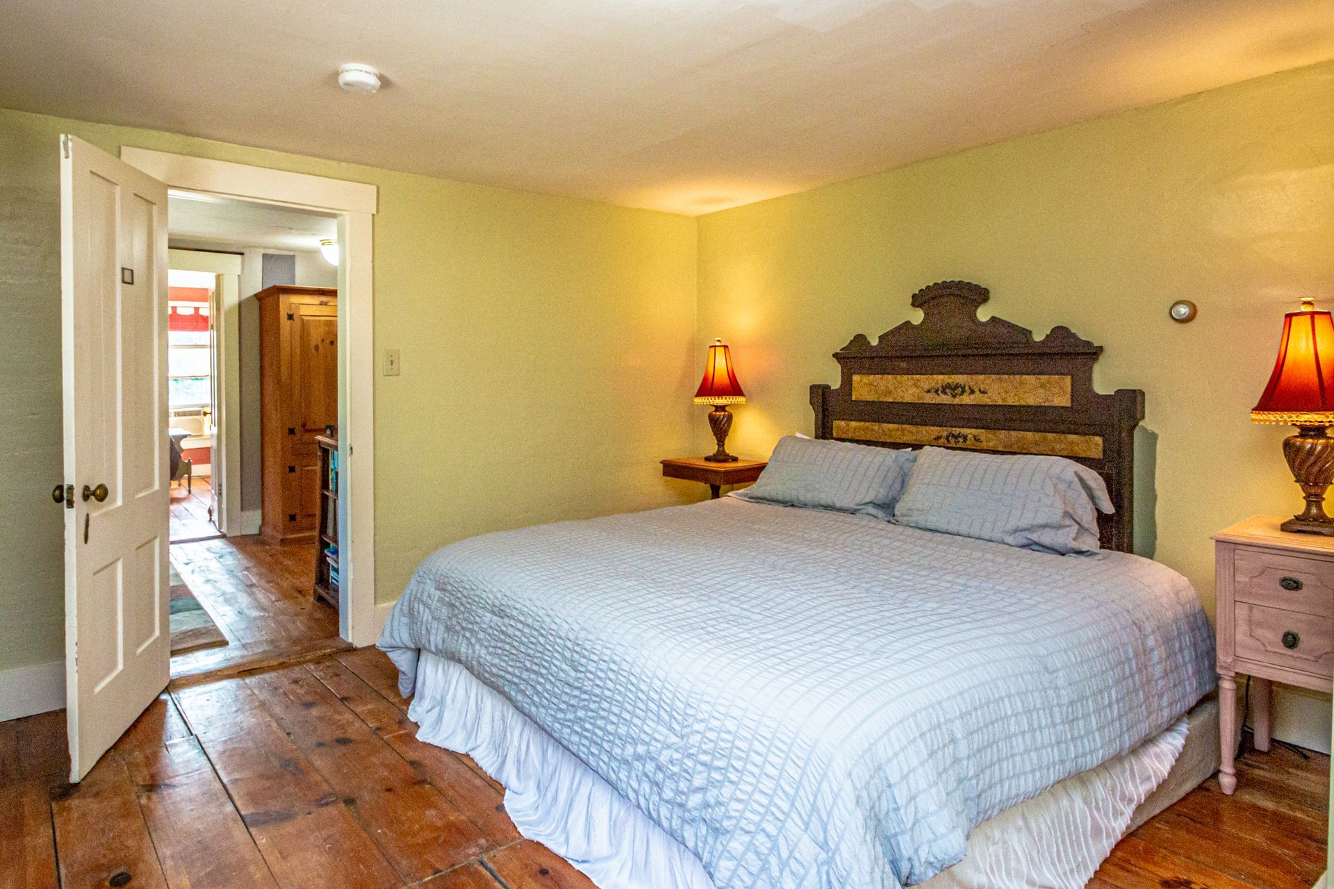 Bedroom with bed, nightstands, and doorway to another room, hardwood floors, light green walls.
