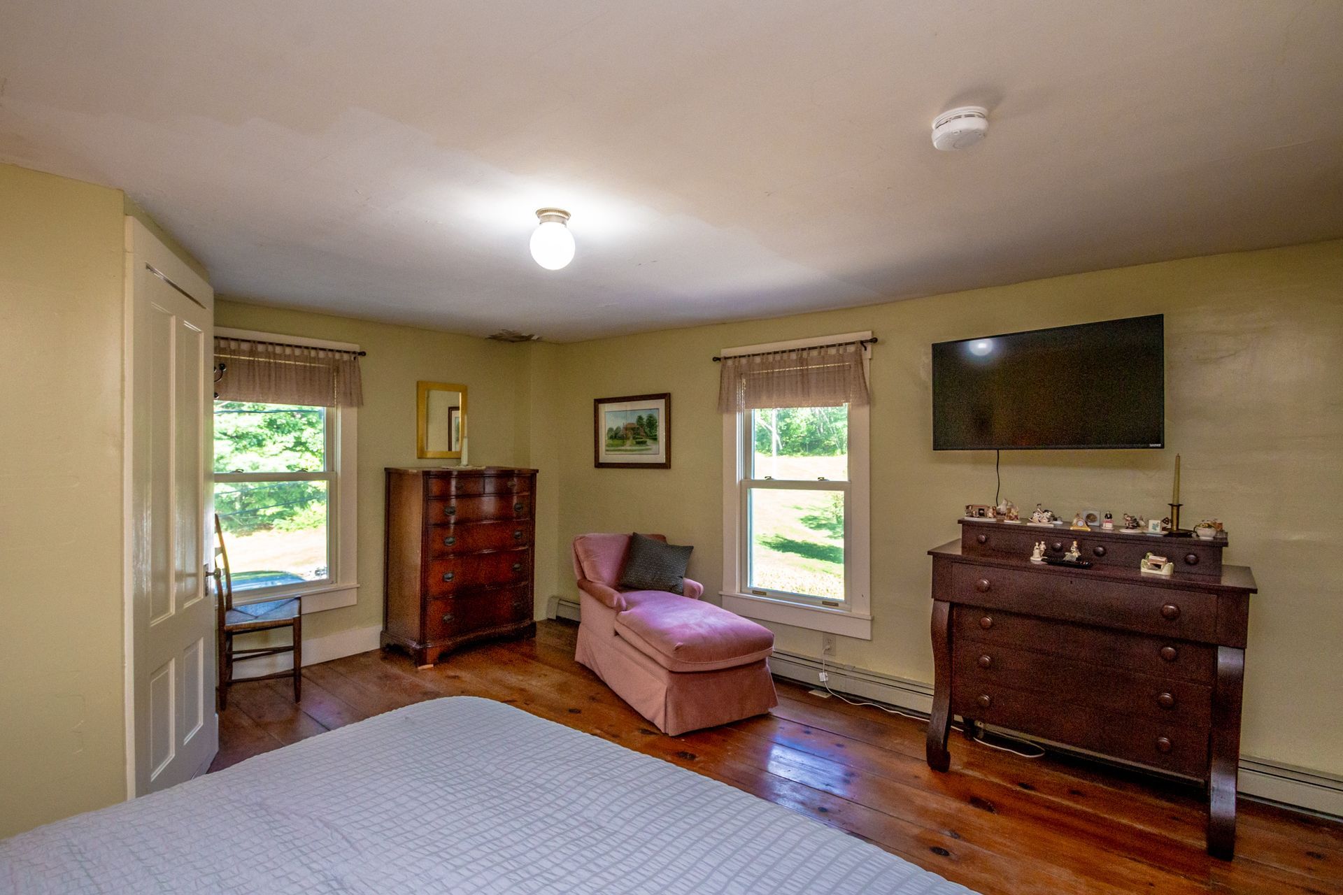 Bedroom with hardwood floor, two dressers, pink chaise lounge, and a window.