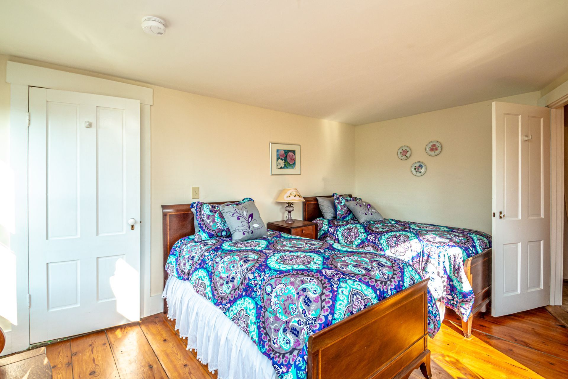 Bedroom with two twin beds, patterned bedding, wooden furniture, and two white doors.