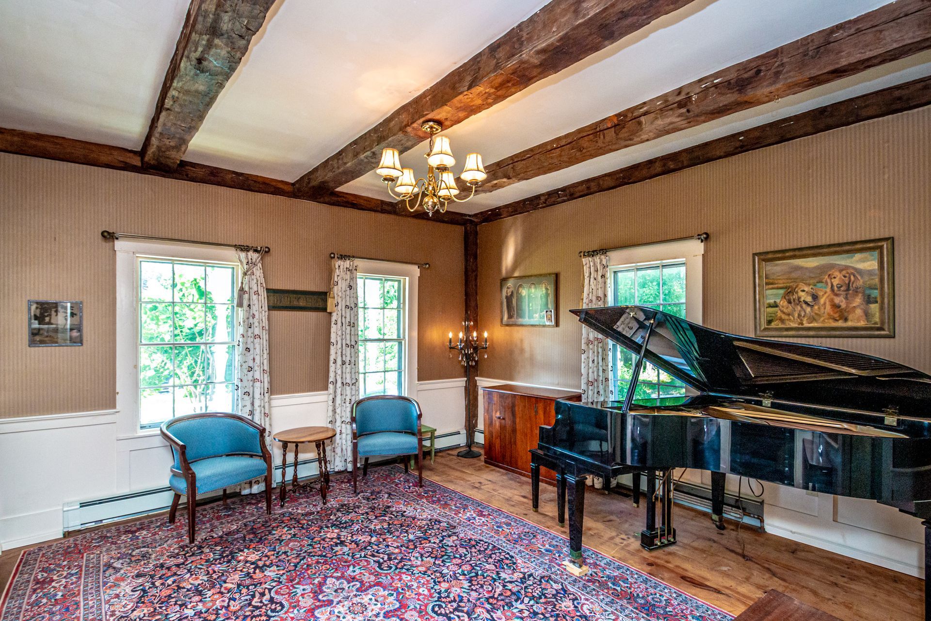 Room with grand piano, two blue chairs, and ornate ceiling beams.