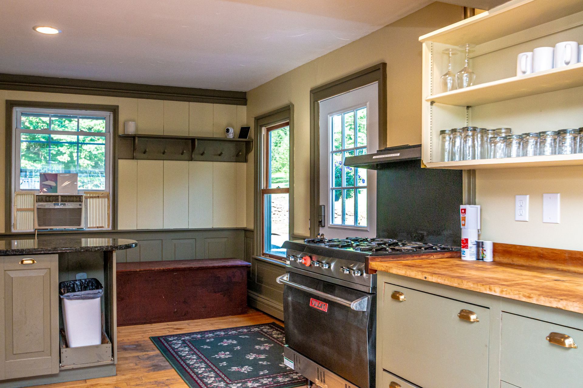 Kitchen with light green cabinets, wood countertop, stainless steel stove, and windows.
