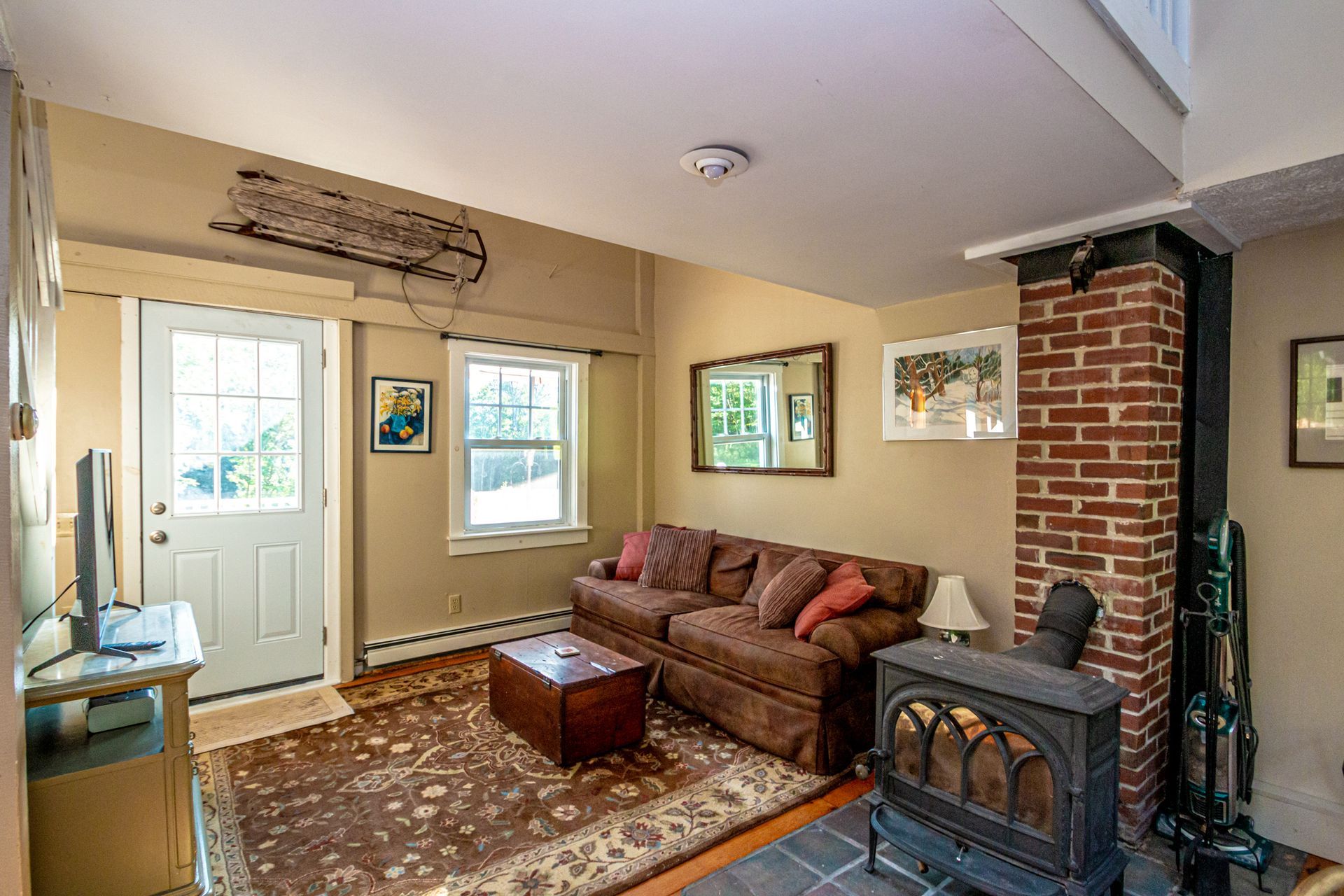 Cozy living room with brown sofa, brick fireplace, wood stove, and door to outside.
