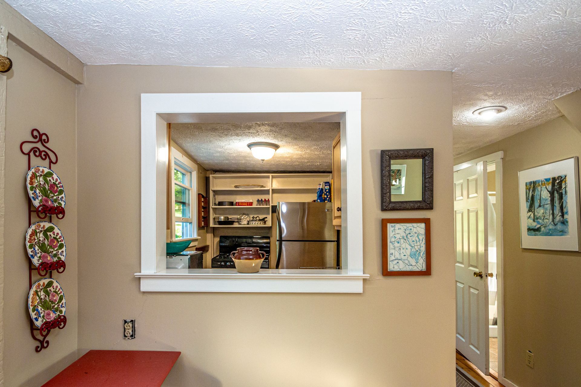 Kitchen pass-through with white trim, looking into a kitchen with stainless steel appliances. Beige walls.