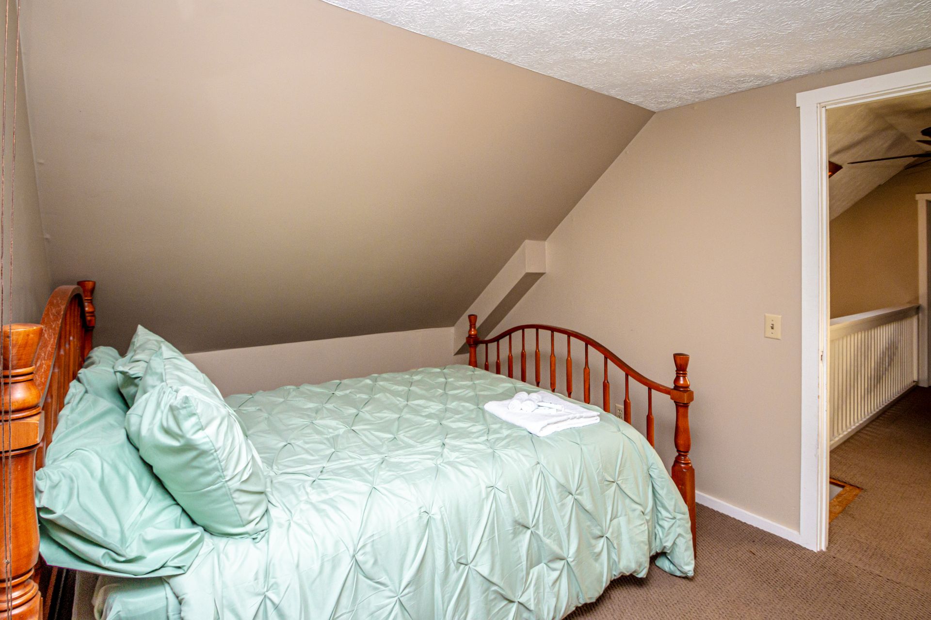 Bedroom with a bed, light green bedding, and a doorway. Beige walls and carpet.