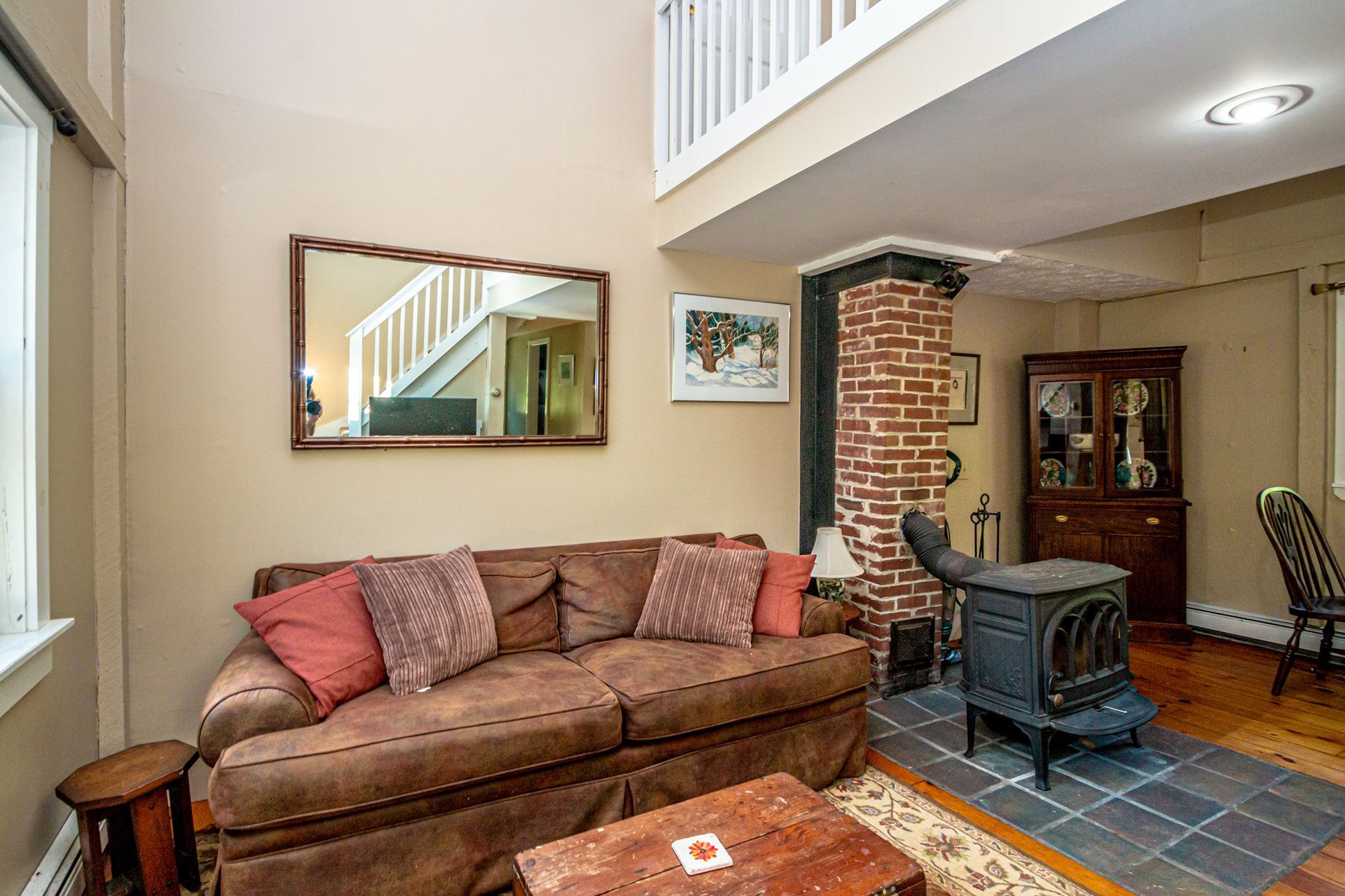 Cozy living room with a brown sofa, fireplace, and a mirror reflecting stairs.