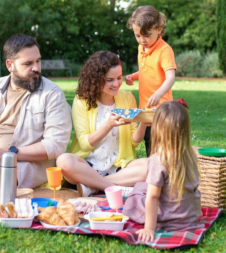 A large family is sitting at a table eating food and drinking wine.