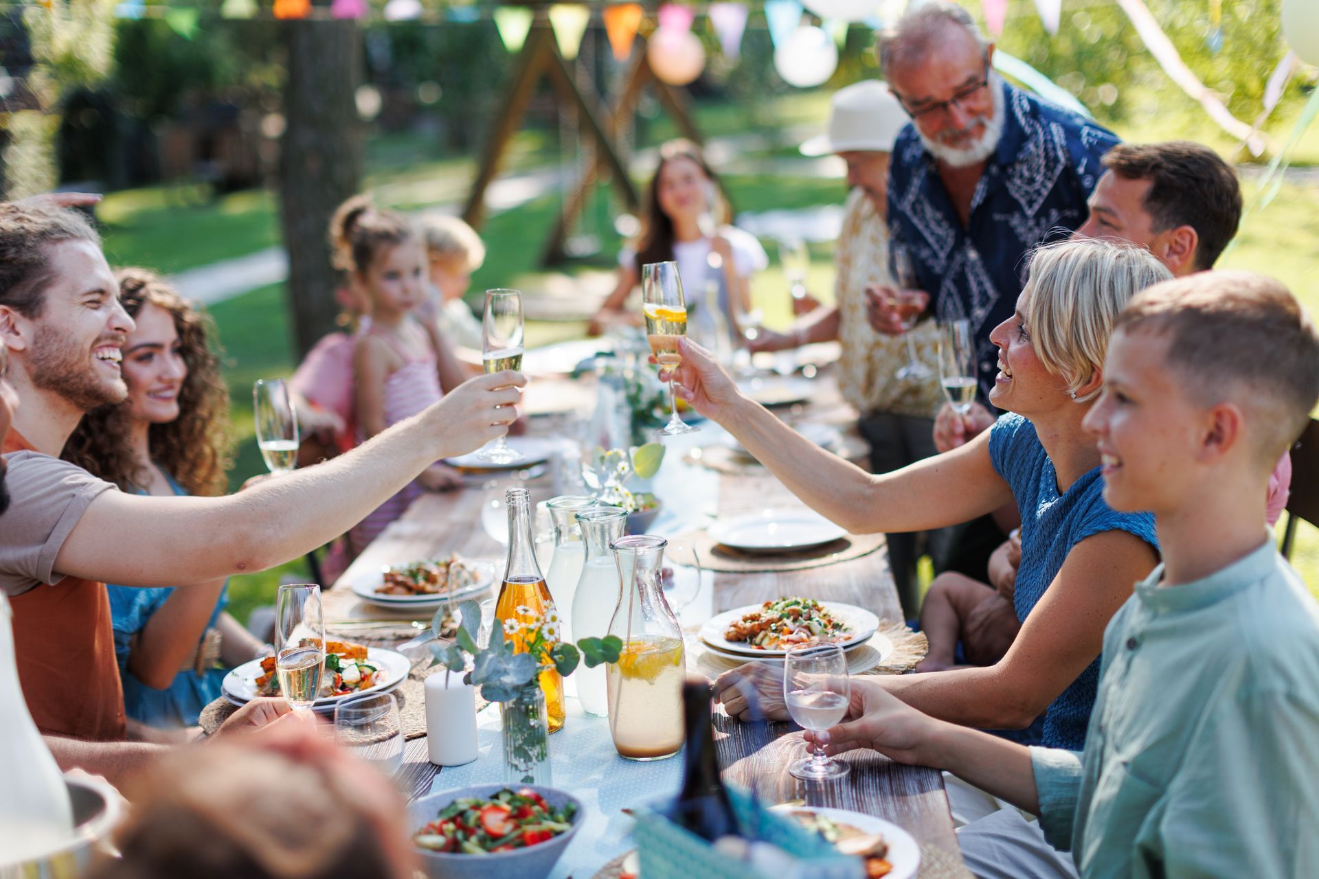 A large family is sitting at a table eating food and drinking wine.