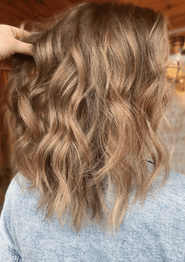Hair salon stylist runs fingers through wavy brown new haircut and color
