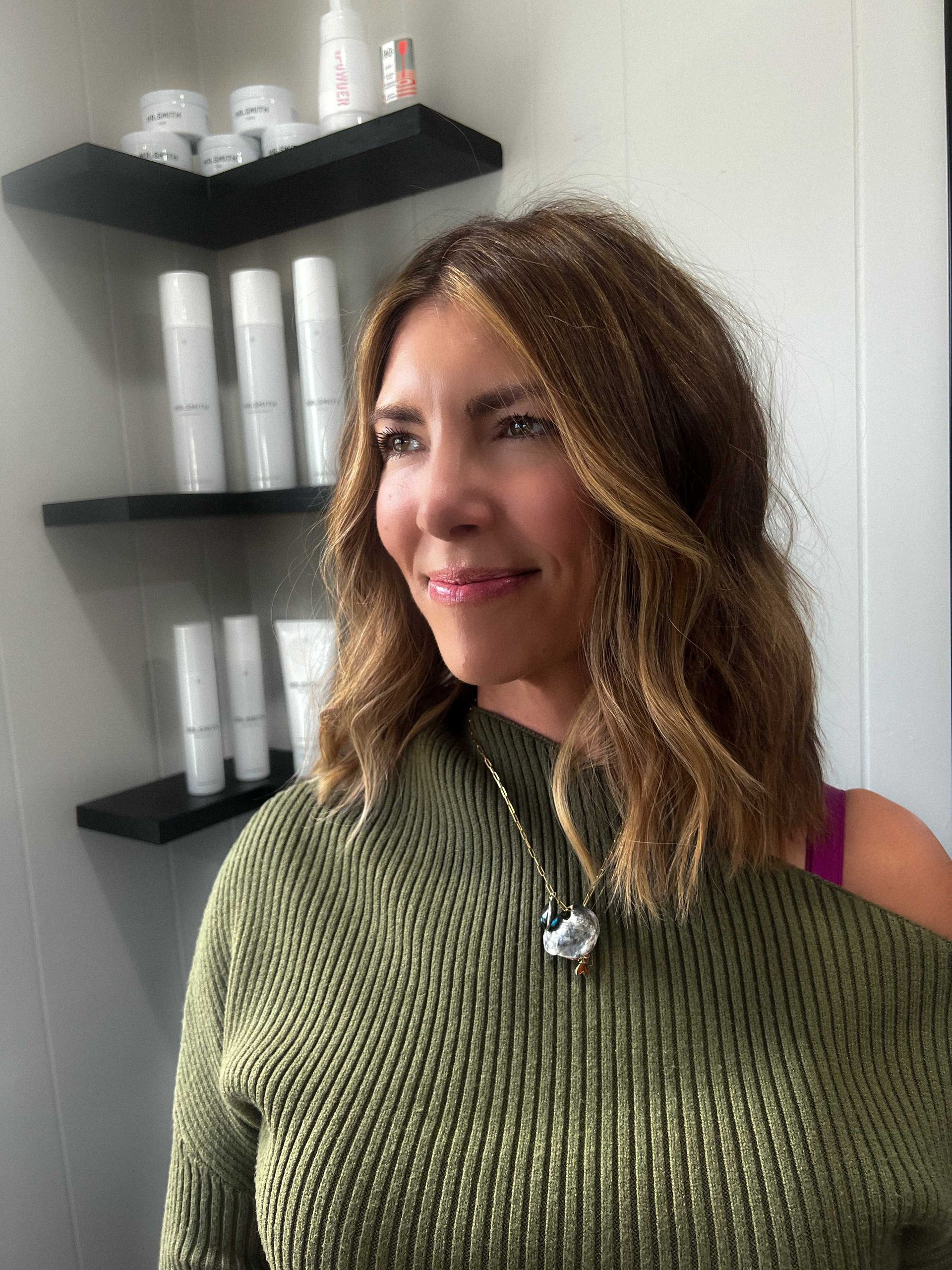 woman in hair salon smiling with new hair style and hair products on shelf