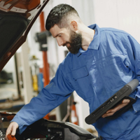 Mechanic in blue coveralls inspecting a car engine in a workshop