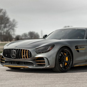 Silver Mercedes sports car parked on pavement with yellow accents and blurred trees in the background