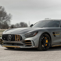 Silver Mercedes sports car parked on pavement with yellow accents and blurred trees in the background