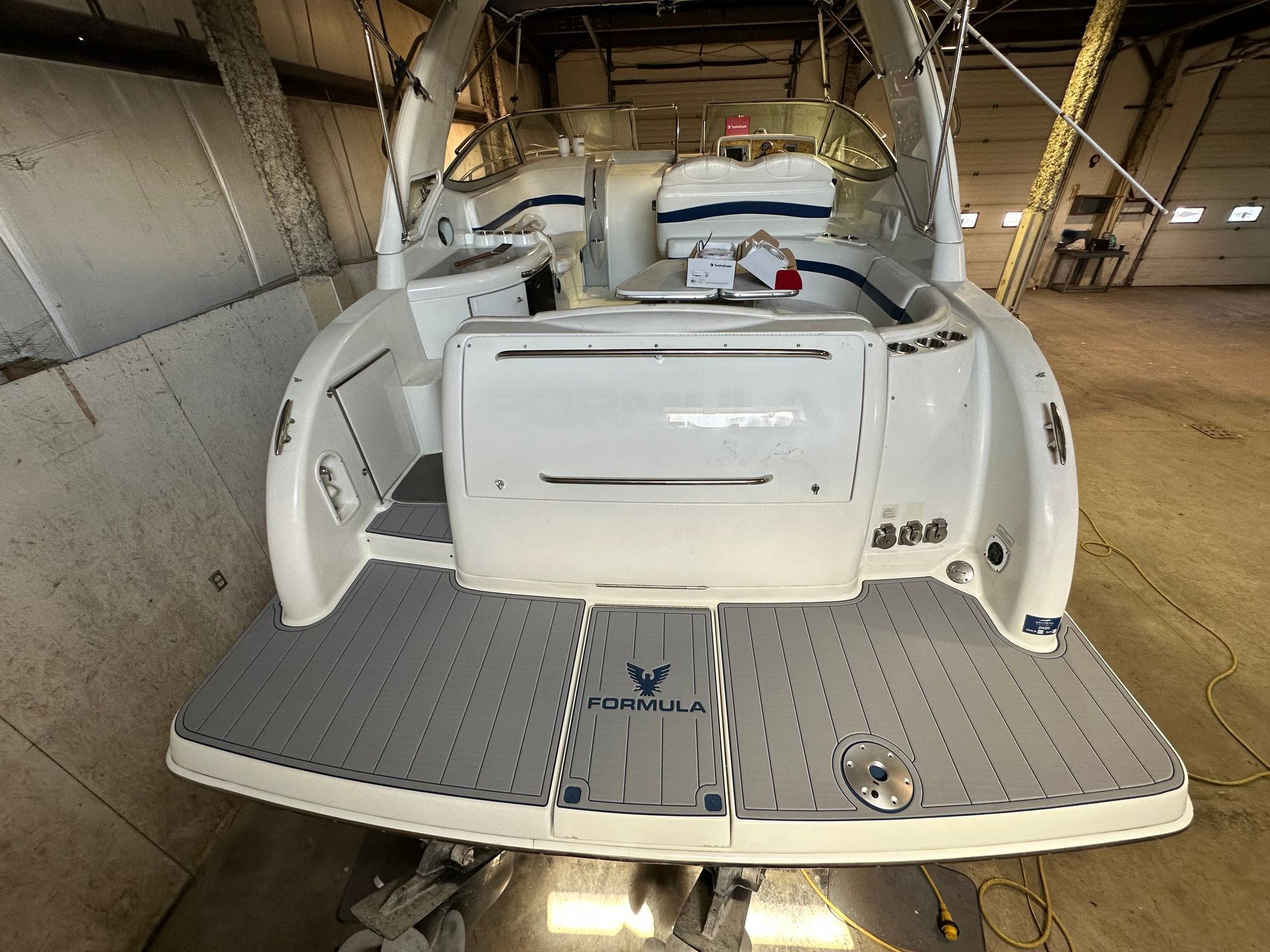 The back of a white boat is sitting in a garage.