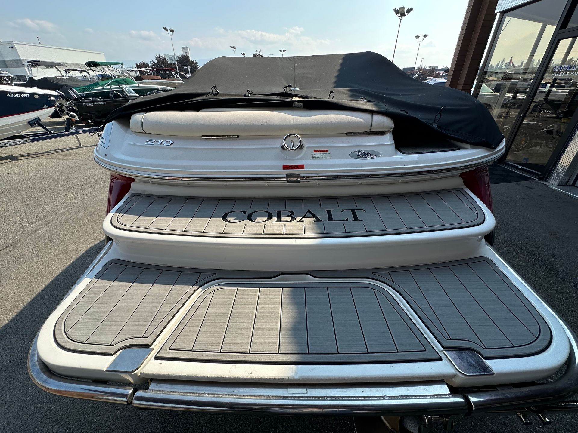The back of a boat with a cover on it is parked in a parking lot.
