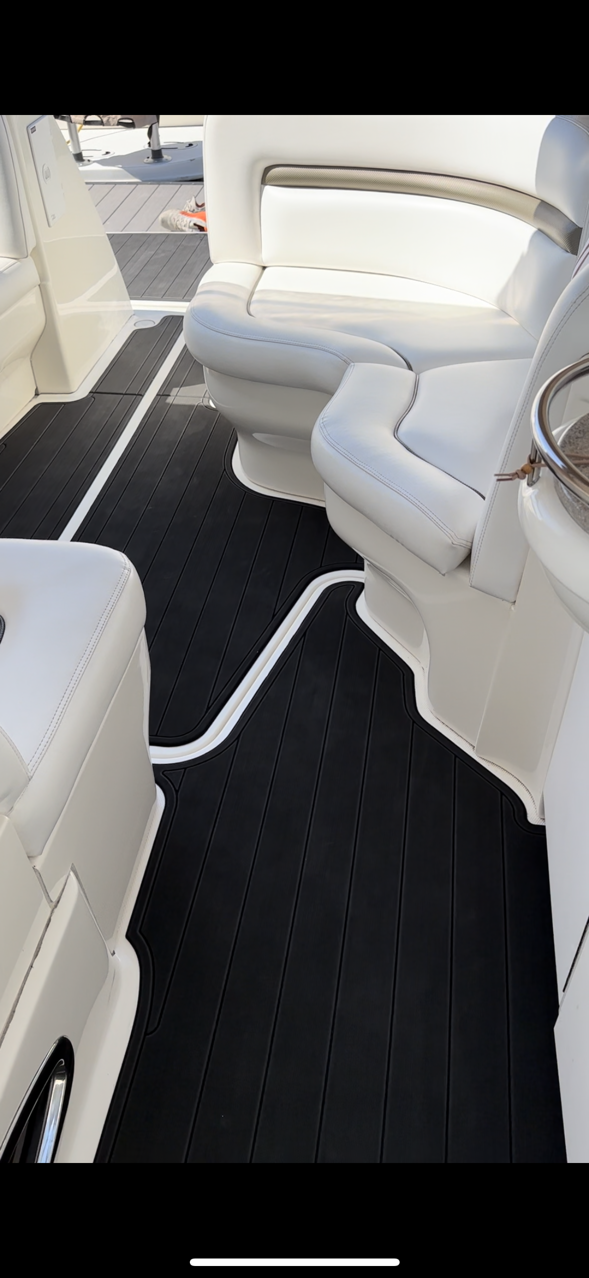 The inside of a boat with a black carpet and white seats.