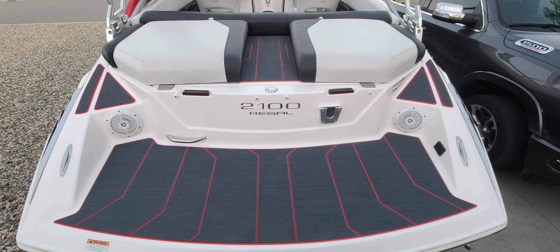 A boat is parked next to a car on a gravel road.